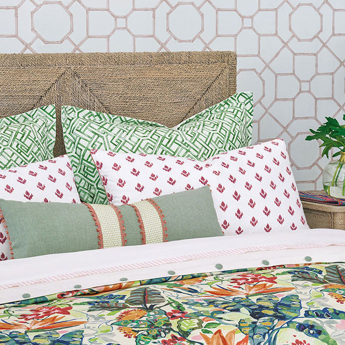 A bed dressed in a tropical floral print duvet cover and coordinating pillows, styled in a bedroom setting with a wooden headboard, nightstand, and patterned wallpaper.