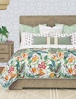 A bed dressed in a tropical floral print duvet cover and coordinating pillows, styled in a bedroom setting with a wooden headboard, nightstand, and patterned wallpaper.